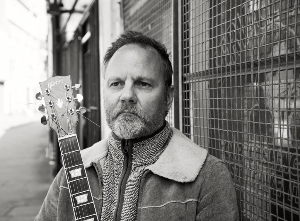 Matt Clark holding a guitar outside on the street